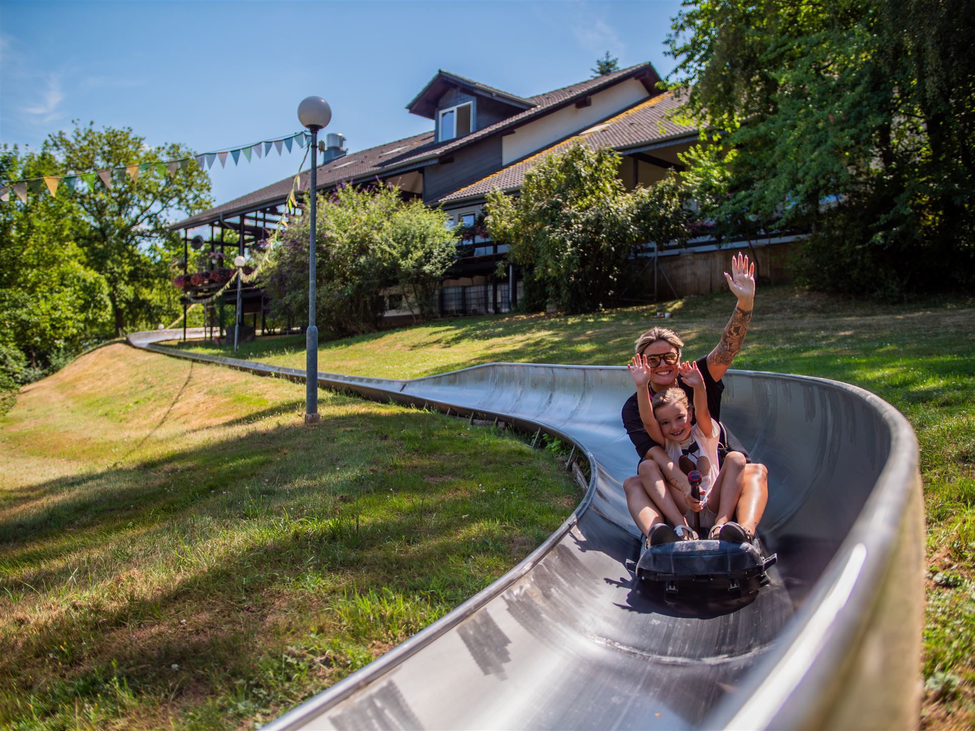 Kind und Begleitung winken auf der Sommerrodelbahn