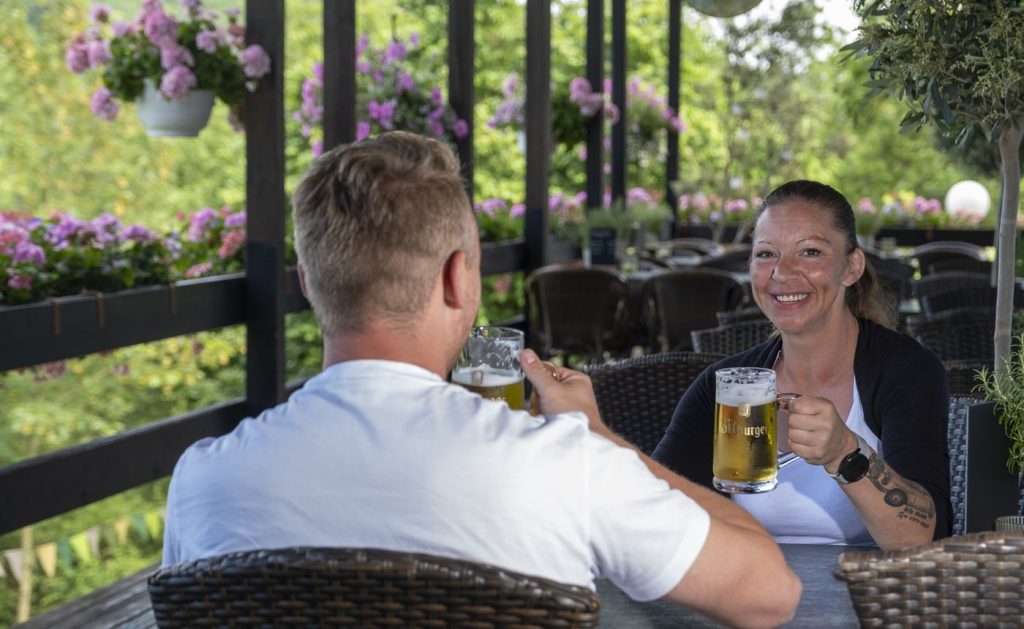 Zwei Gäste stoßen auf der Sonnenterrasse des Restaurants Eifeltor mit Bier an